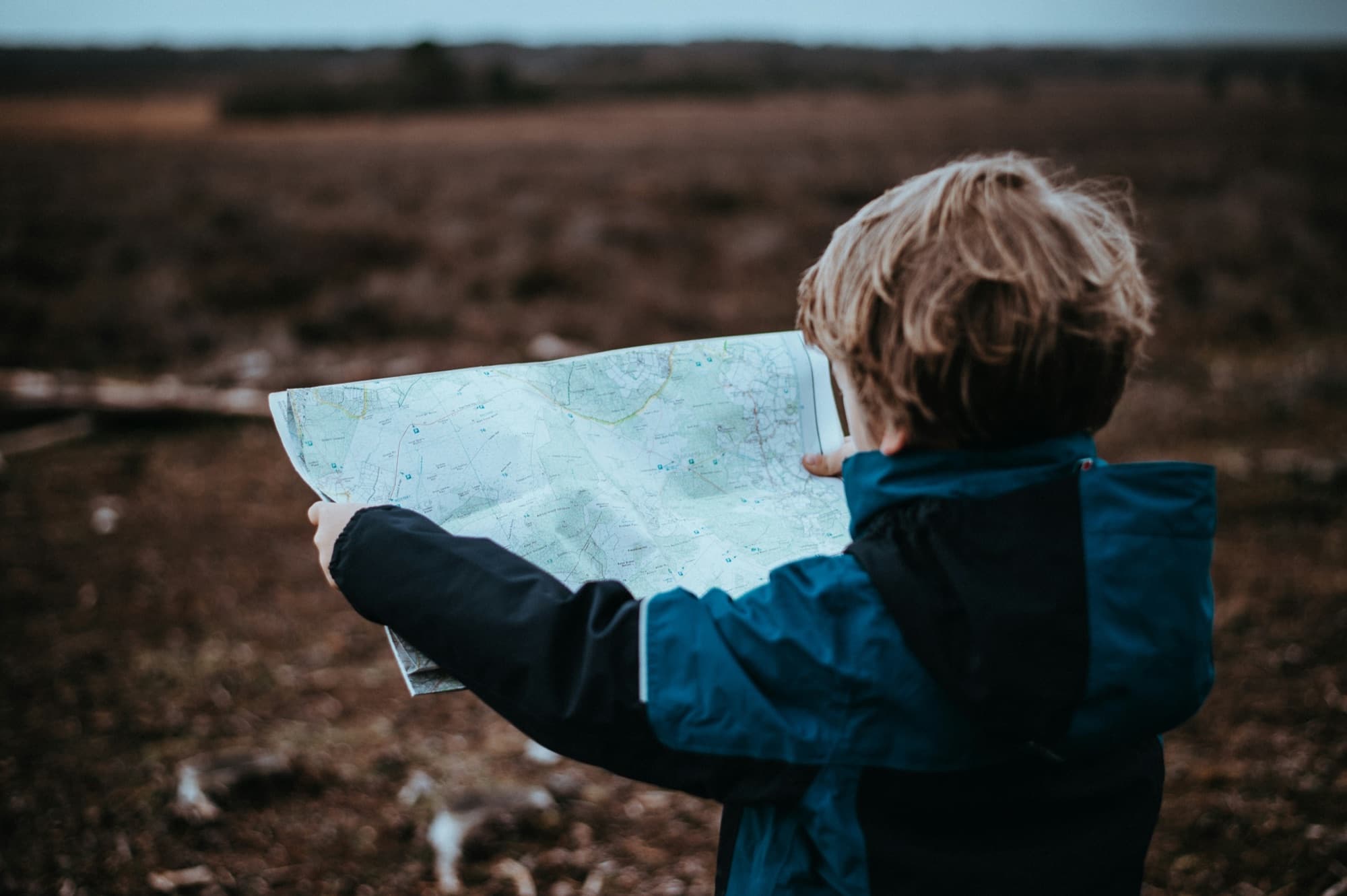 A young child in a blue jacket studying a folded map in an open field