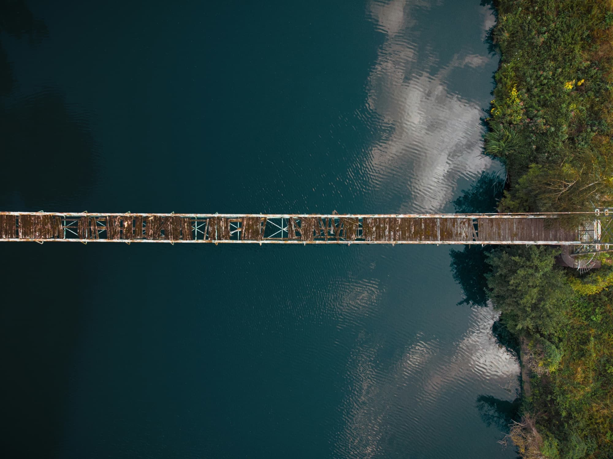 Aerial view of a long, narrow wooden footbridge stretching across a still, deep-green lake